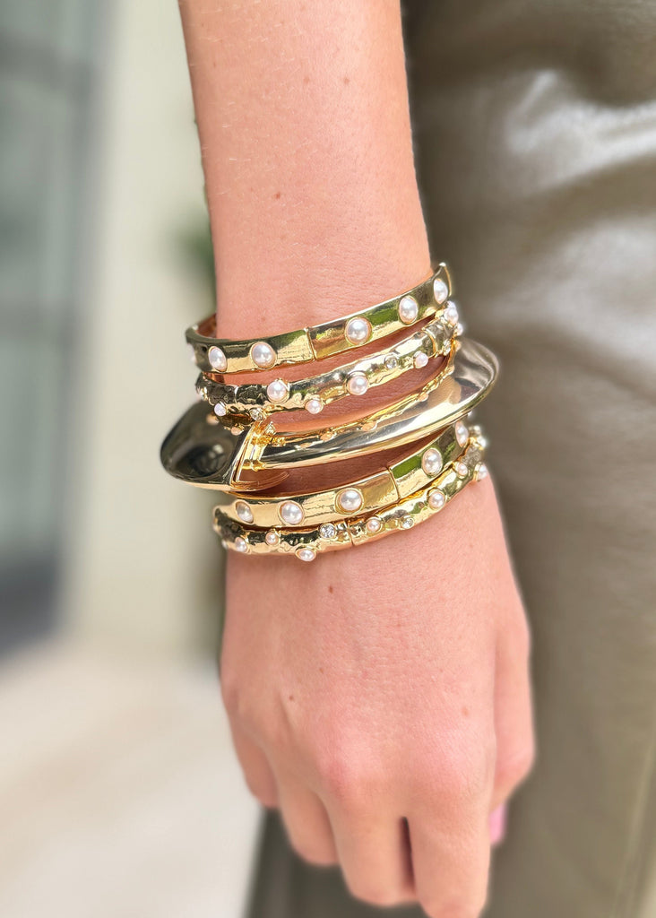 Hand wearing multiple gold bracelets with a blurred background
