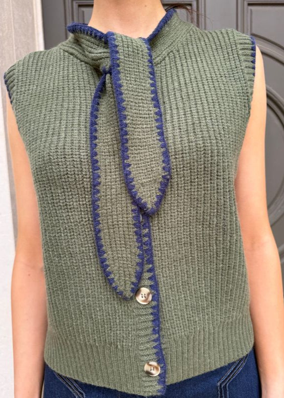 Green knitted vest with blue trim worn by a person, against a neutral background