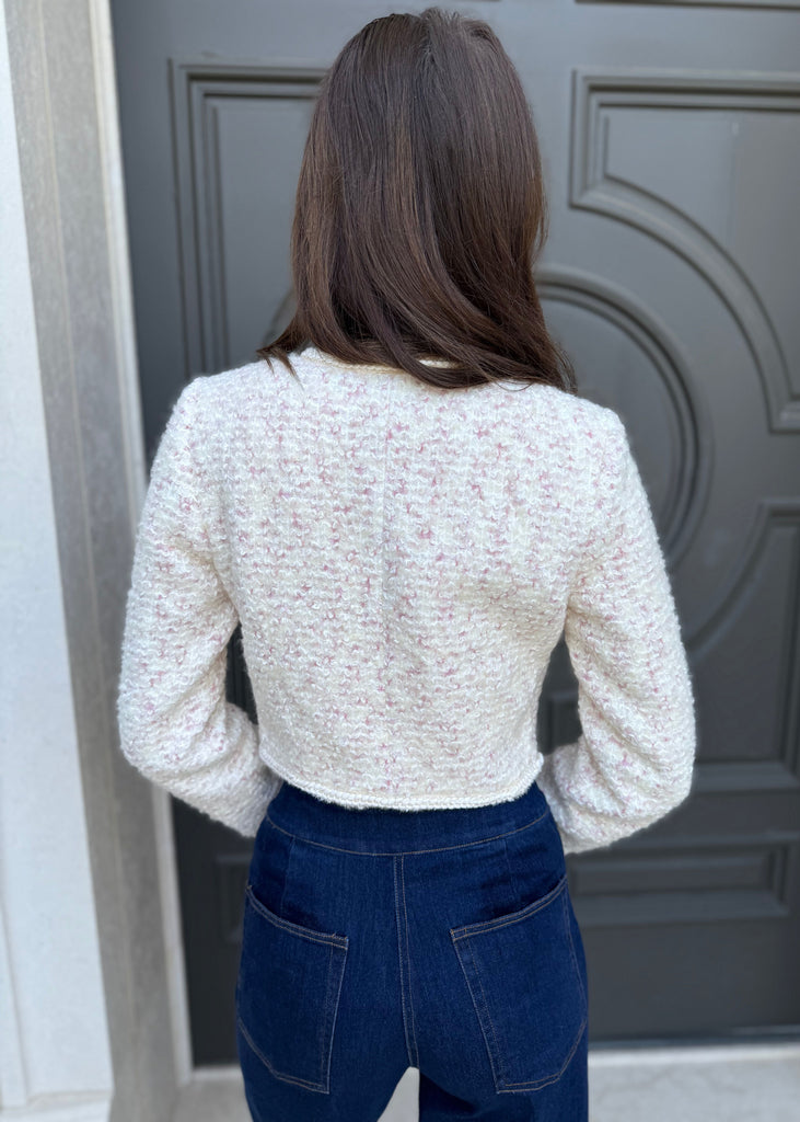 Person wearing a textured white top and blue jeans standing in front of a gray door.