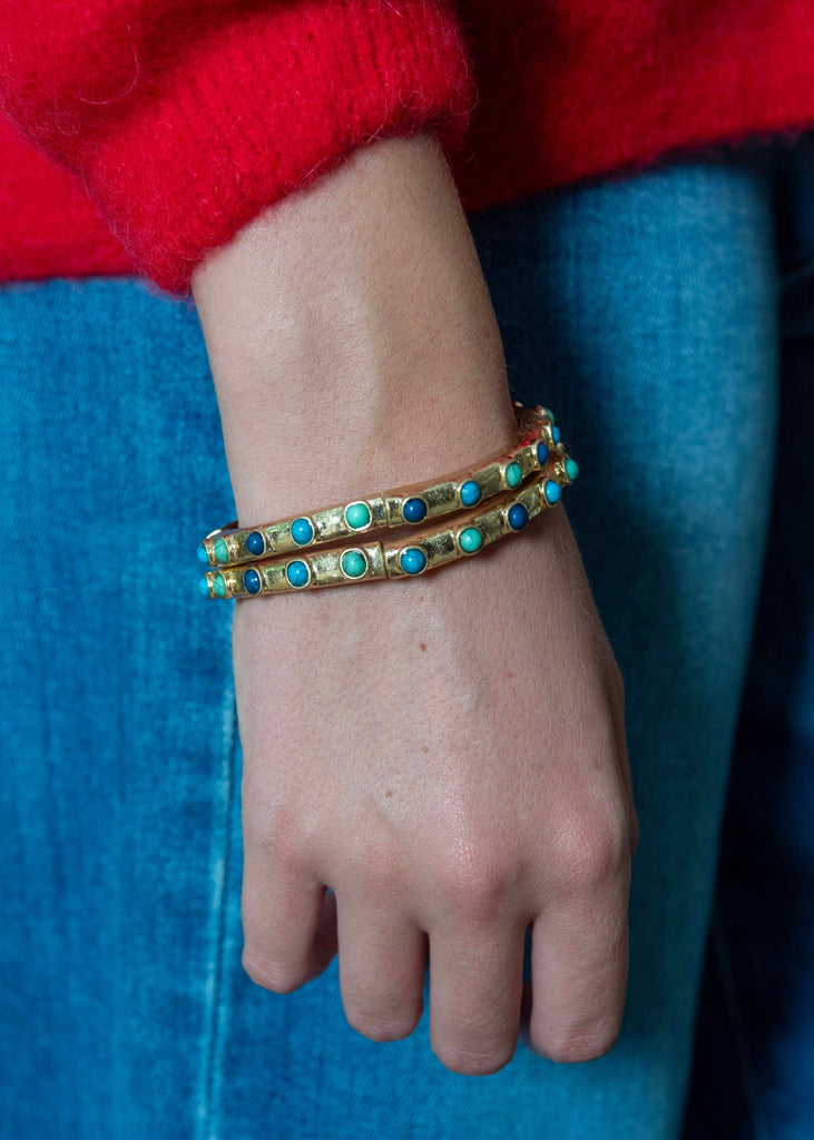 Close-up of a wrist wearing gold and turquoise bracelets against a blue background.