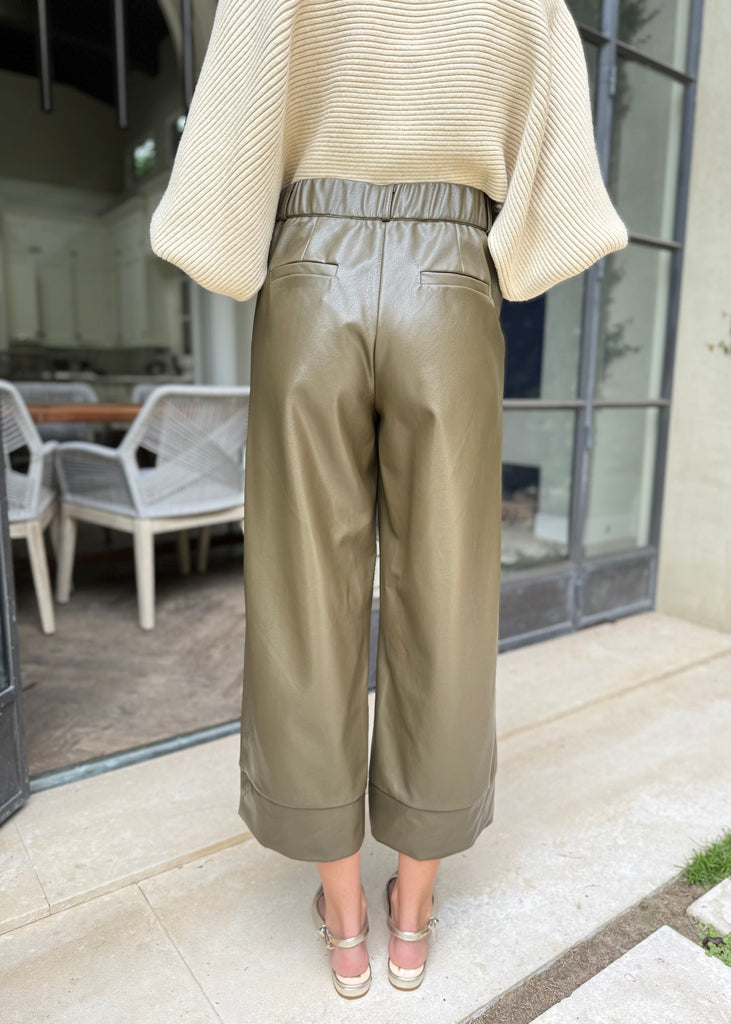 Person wearing olive green pants and a beige sweater outdoors.