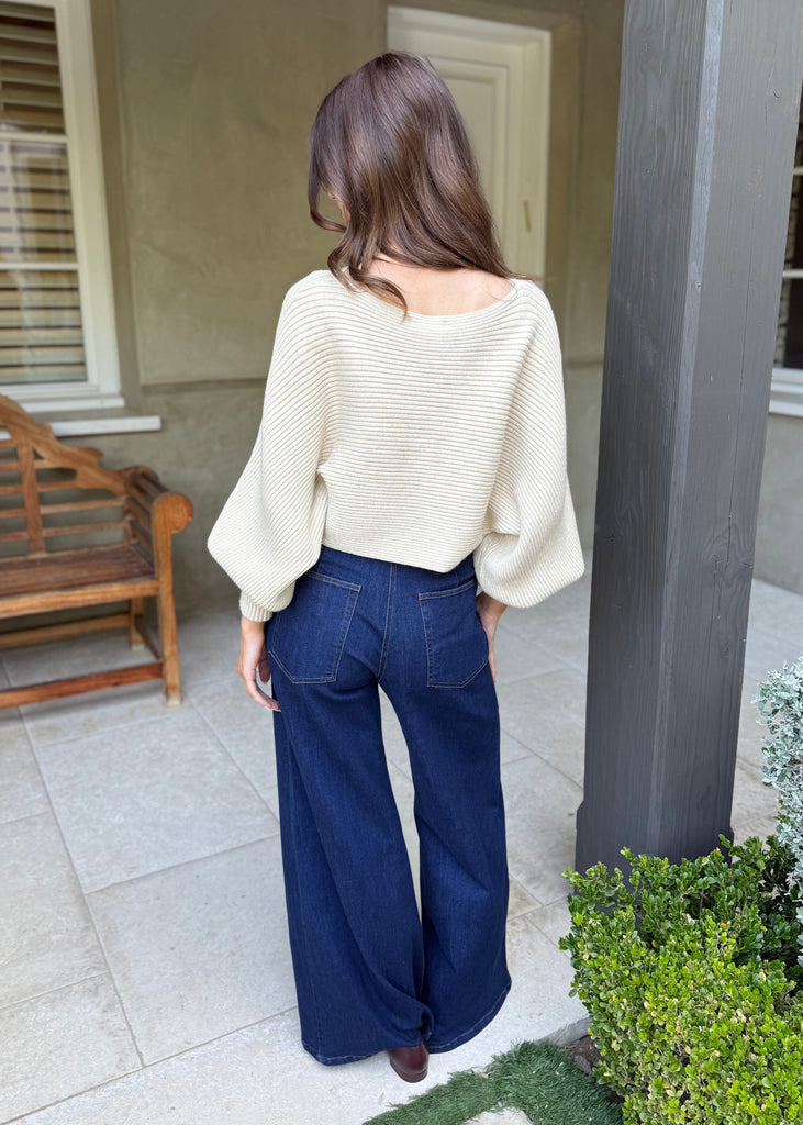Person wearing a white blouse and blue jeans standing on a patio.