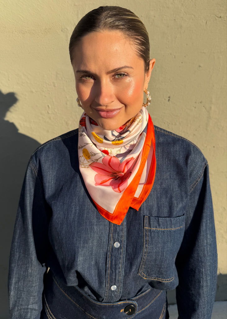 Woman wearing a floral scarf with an orange border against a beige wall