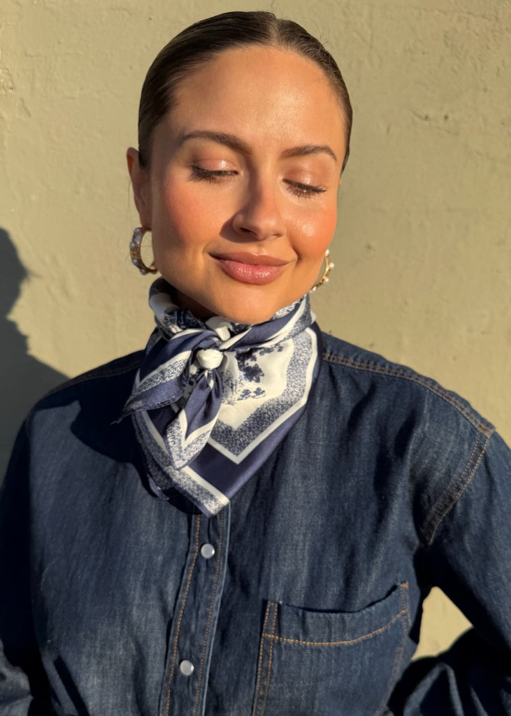 Woman wearing a denim jacket and scarf against a plain background