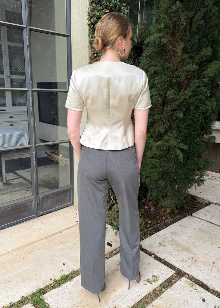 Person wearing a beige blouse and gray pants standing outdoors on a stone patio.