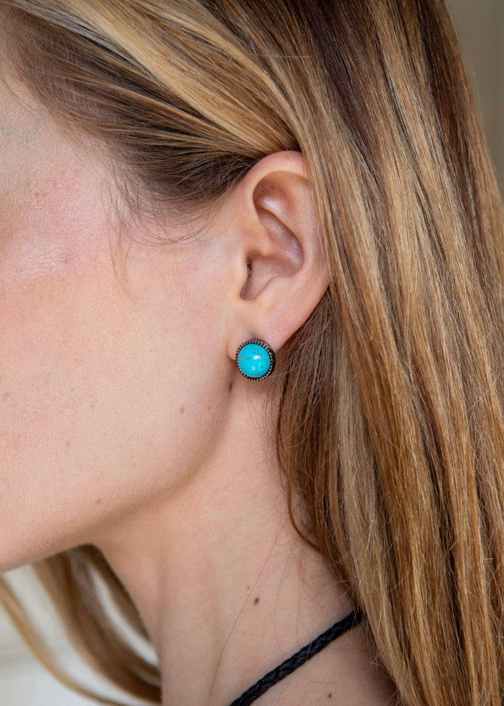 Close-up of a person wearing turquoise earrings with a neutral background