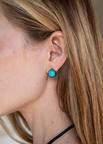 Close-up of a person wearing turquoise earrings with a neutral background