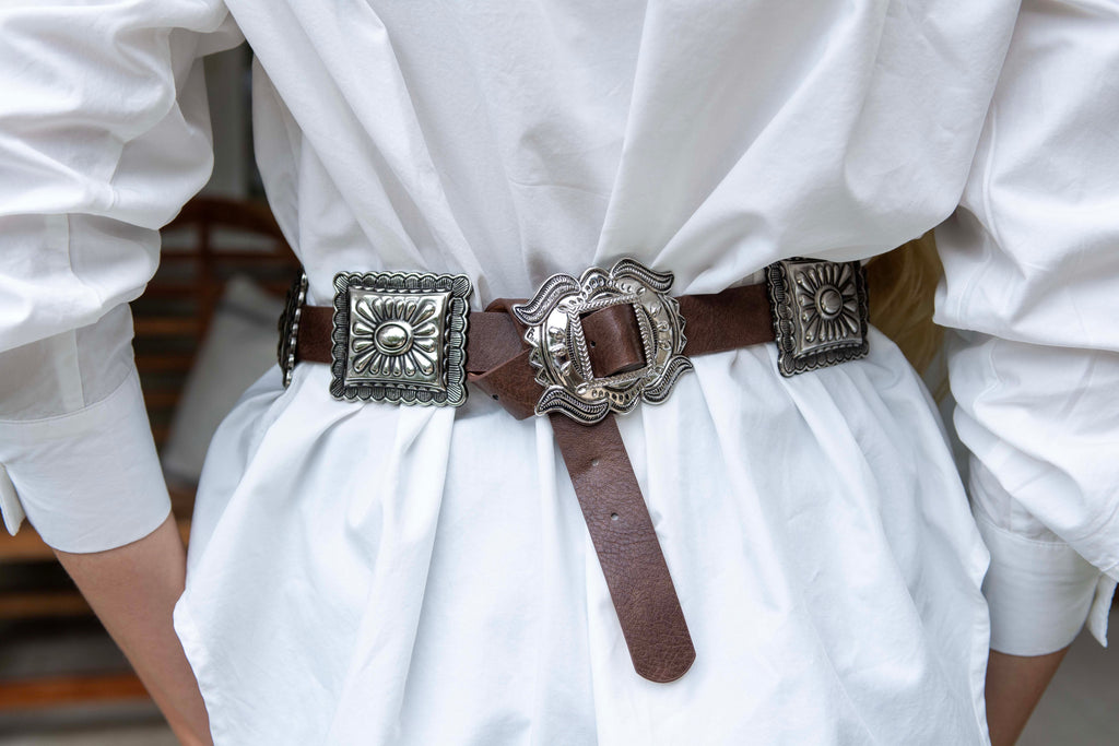 Person wearing a white outfit with a brown belt featuring silver buckles.