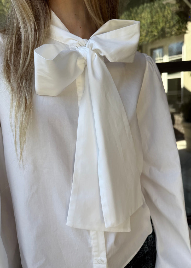 White blouse with a large bow detail on the back, worn by a person.