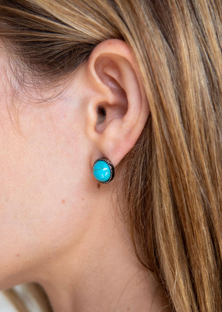 Close-up of a person wearing turquoise stud earrings with a blurred background