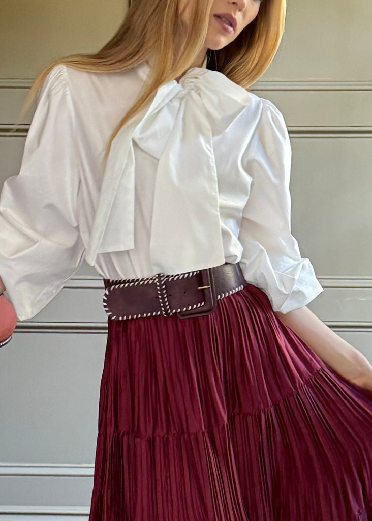 Woman in a white blouse and burgundy skirt standing in a room with wooden paneling and a table with flowers.