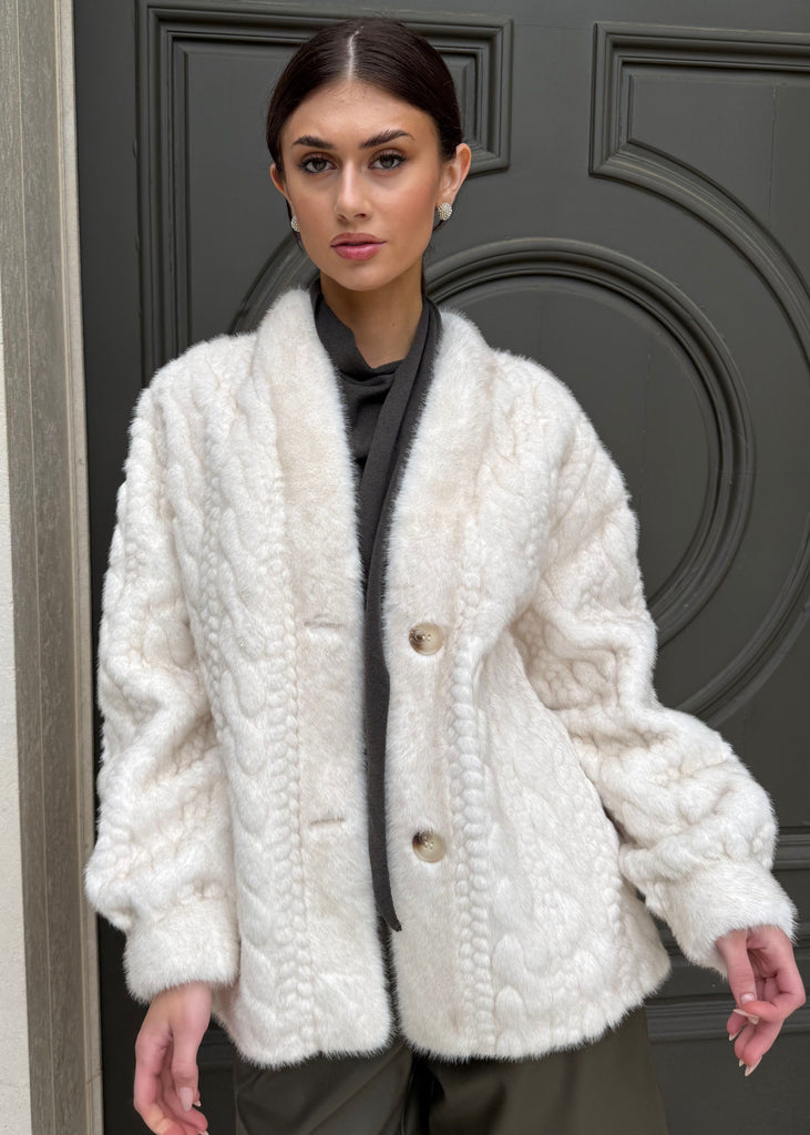 Woman wearing a white textured coat standing in front of a dark door.