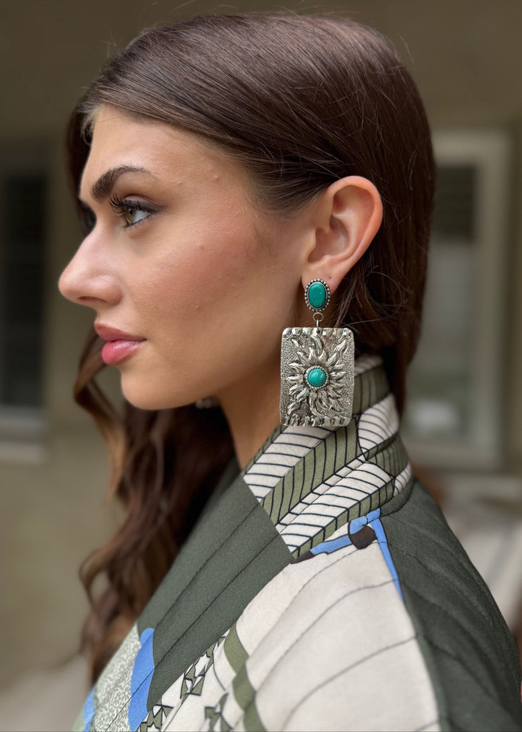 Woman wearing large, ornate earrings with turquoise stones.