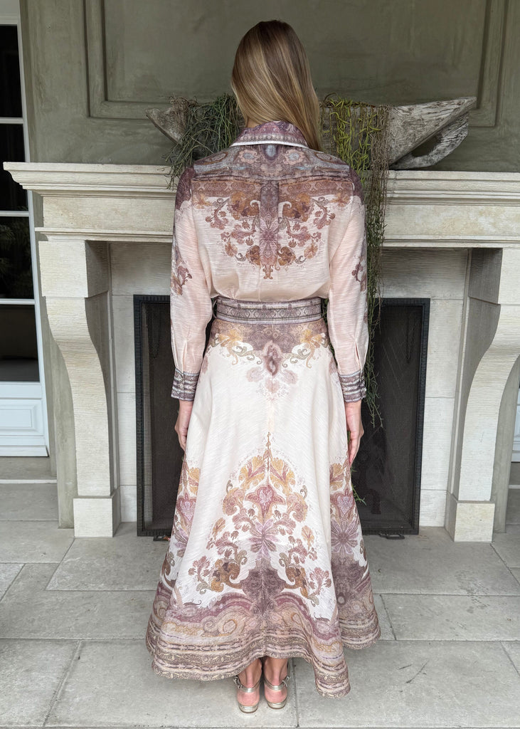 Woman wearing a long, patterned dress standing in front of a stone fireplace.