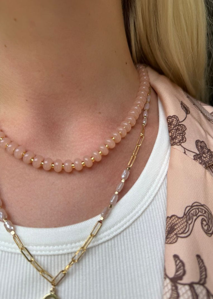 Close-up of a person wearing multiple necklaces with a white top and patterned sleeve.