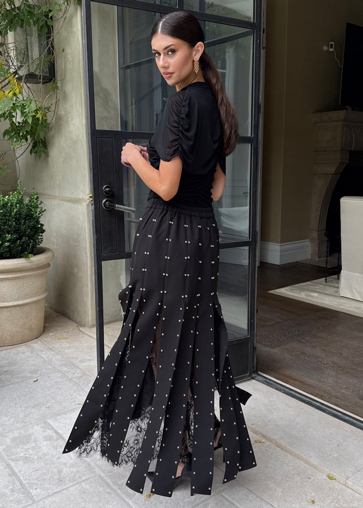 Woman in a black dress with ruffled skirt standing in front of a glass door.