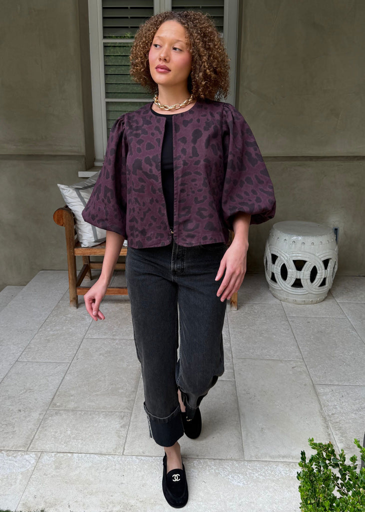 Woman wearing a purple patterned top and dark jeans standing on a patio.