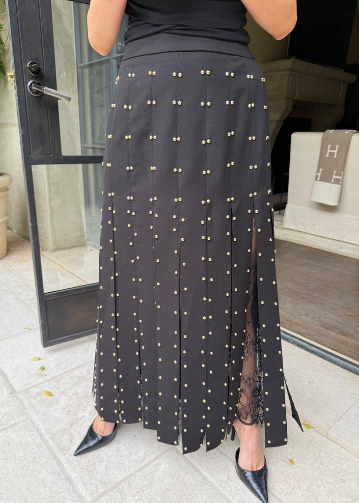 Person wearing a black skirt with gold embellishments in an indoor setting.