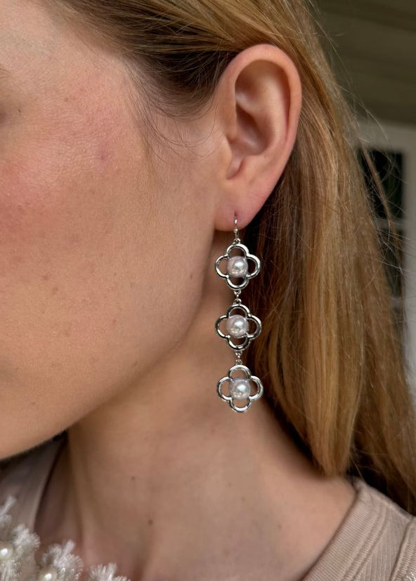 Close-up of a woman wearing silver floral earrings with a neutral background