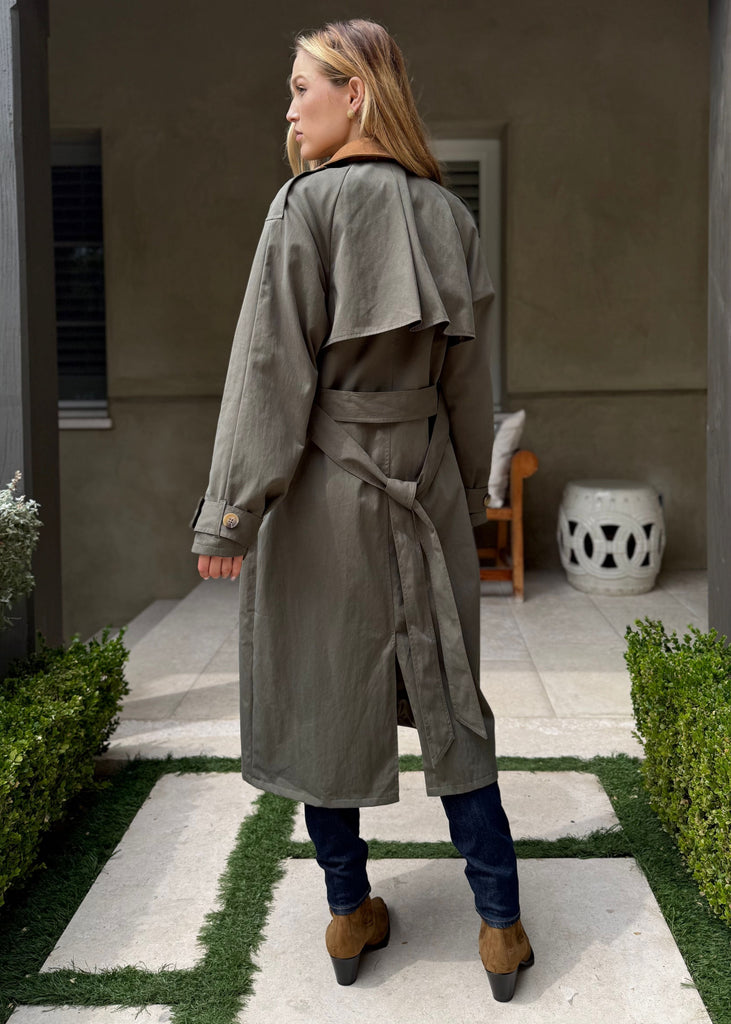 Woman in a long coat walking on a garden path with a building in the background