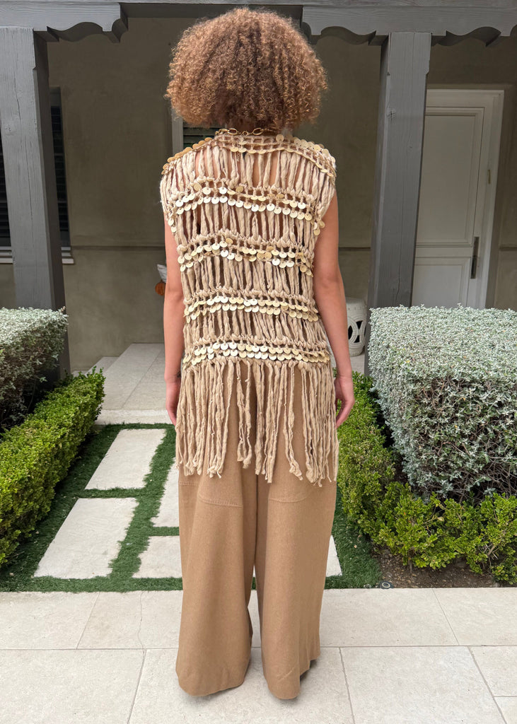 Person wearing a beige sleeveless top with fringe details in an outdoor setting.