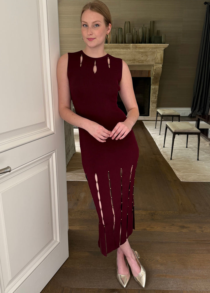 Woman in a burgundy dress standing in a room with wooden flooring and a fireplace.