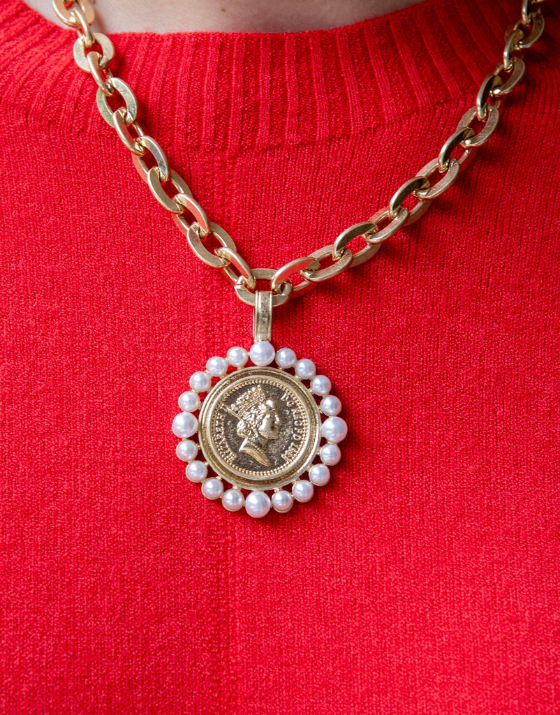 Gold necklace with a round pendant featuring a face design on a red sweater.