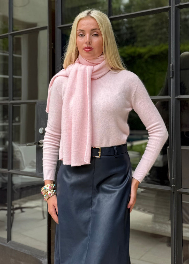 Woman wearing a pink top and blue skirt standing in front of a glass door.