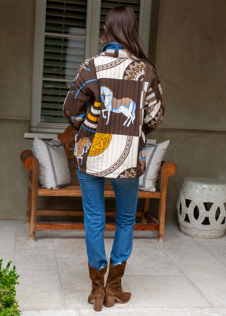 Woman wearing a patterned shirt and blue jeans standing on a patio.