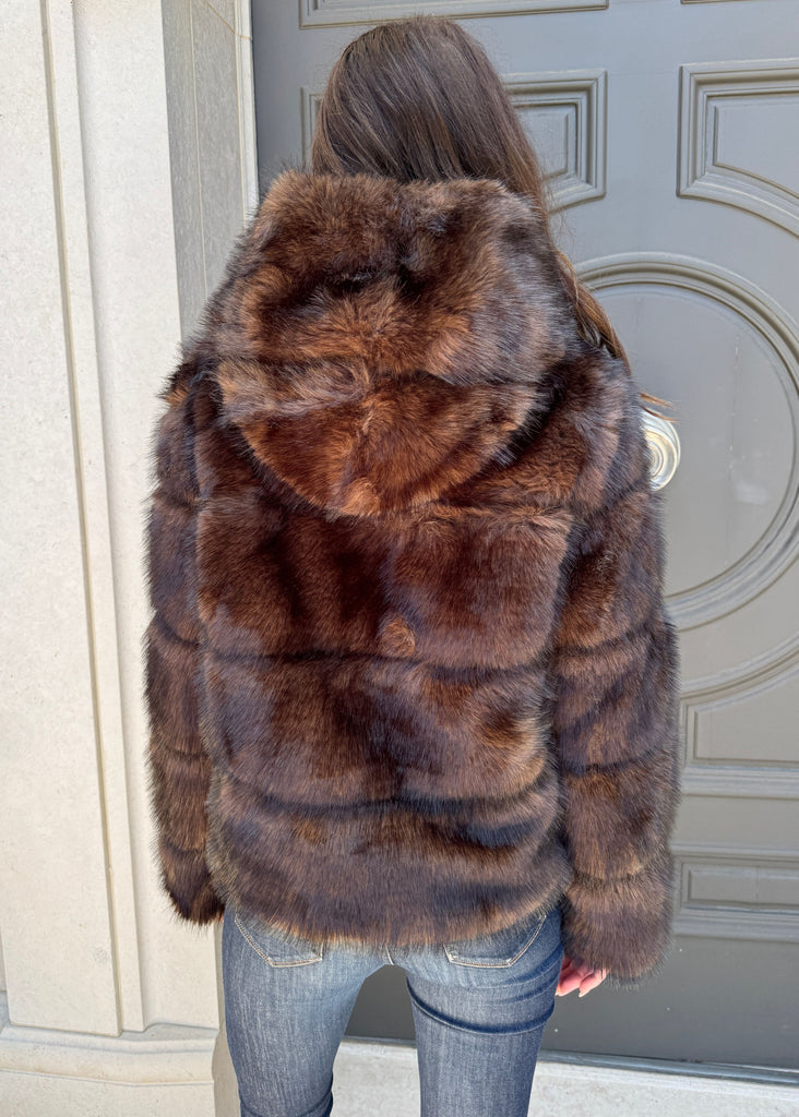 Person wearing a brown fur coat standing in front of a door.