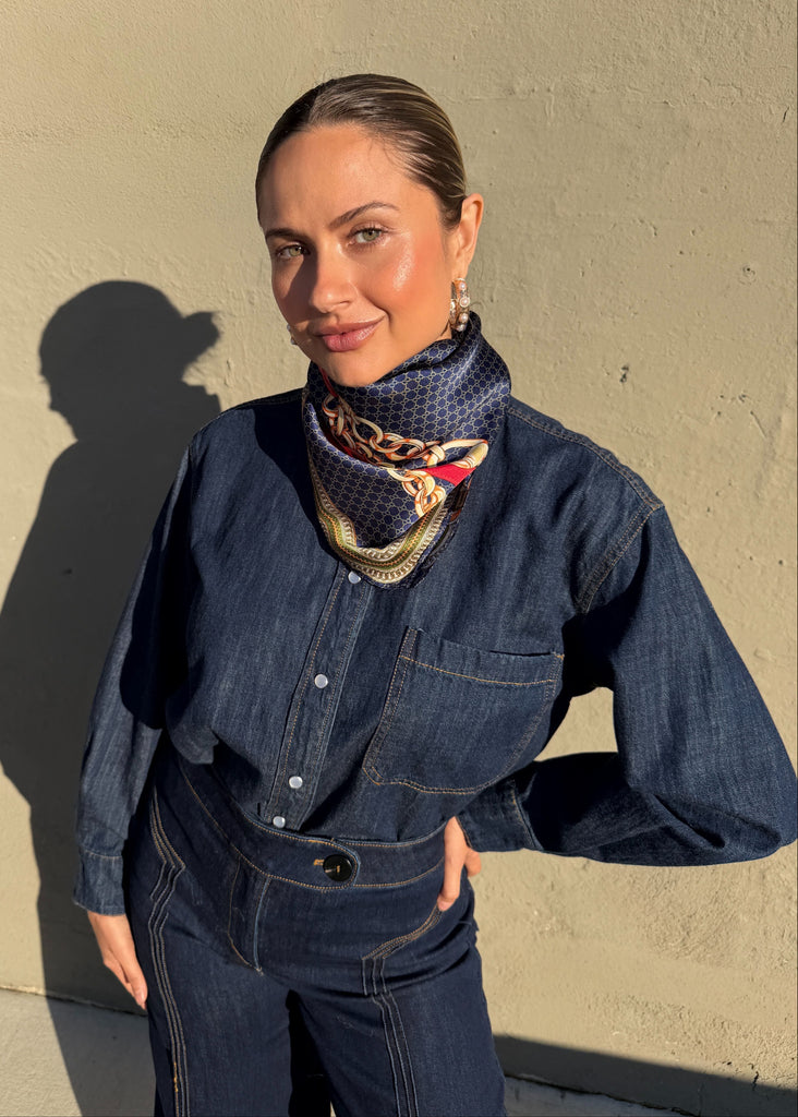 Woman wearing a denim outfit with a scarf against a beige wall