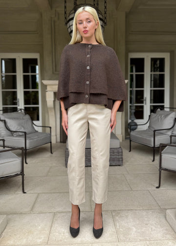 Woman wearing a brown poncho and beige pants in an elegant indoor setting