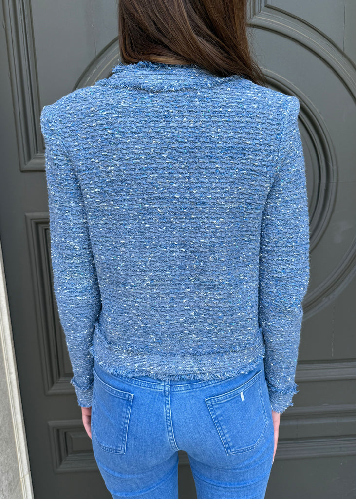 Person wearing a blue textured sweater and jeans standing in front of a gray door.