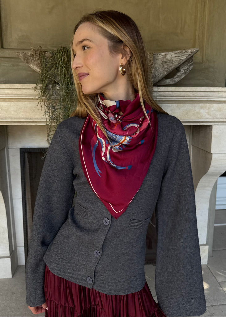 Woman wearing a gray cardigan and red scarf in front of a building.