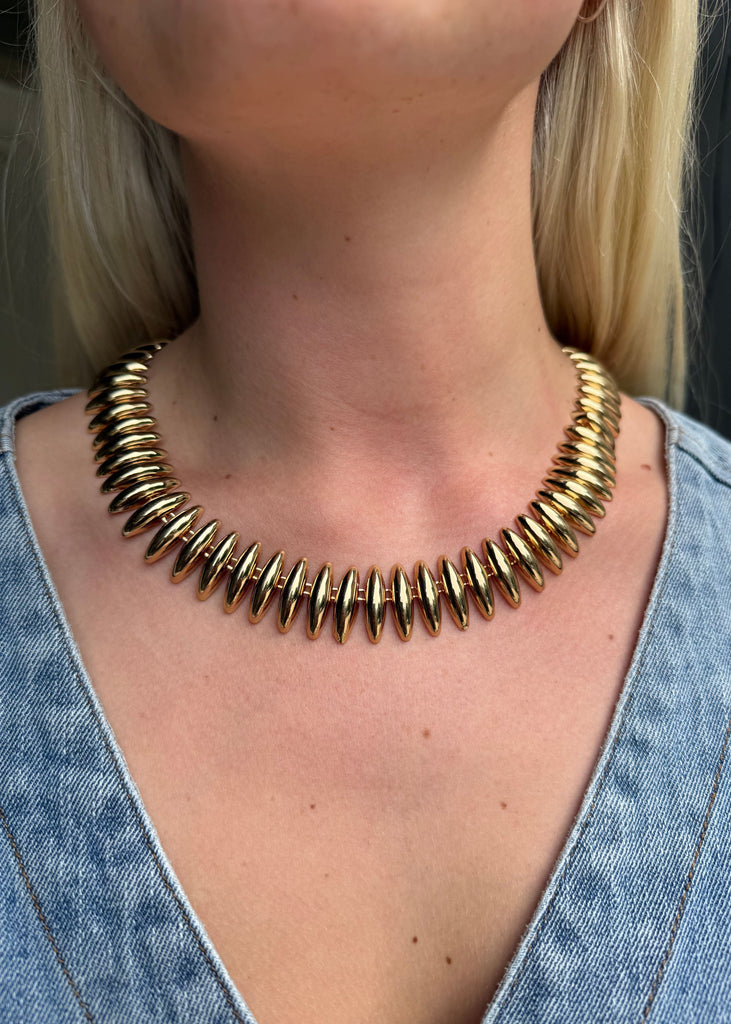 Gold necklace worn by a person with a denim shirt
