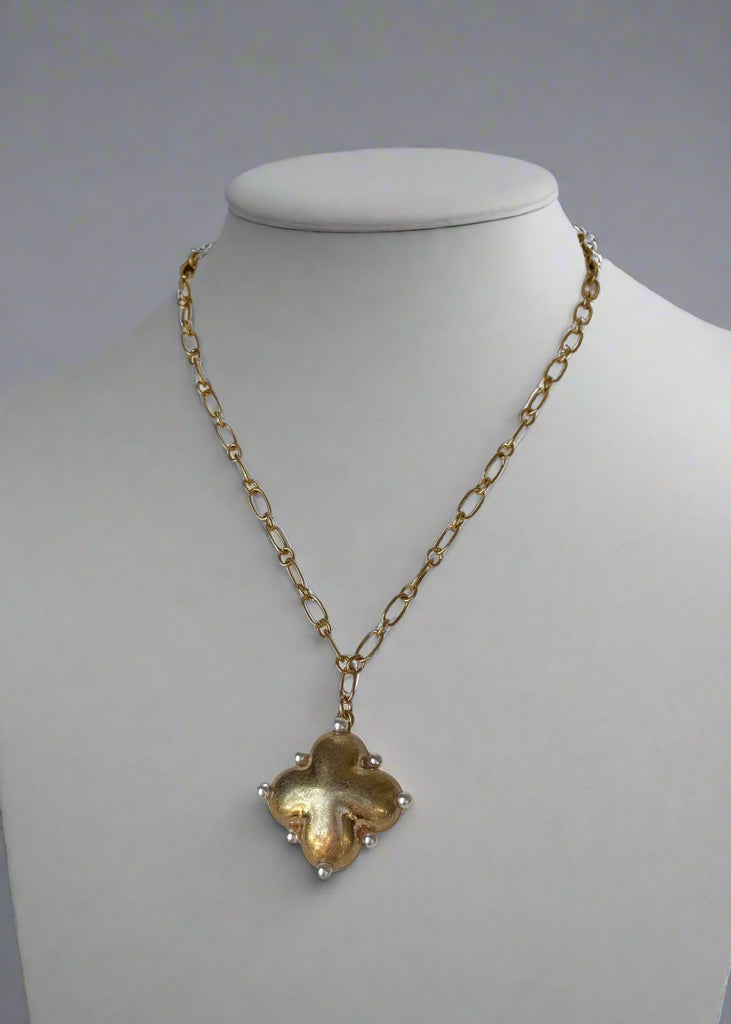 Gold necklace with a clover-shaped pendant on a mannequin.