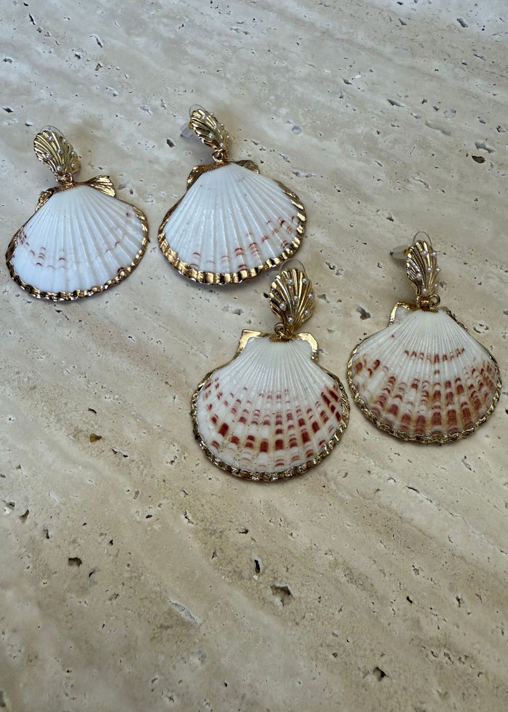 Shell-shaped earrings with gold accents on a textured beige surface