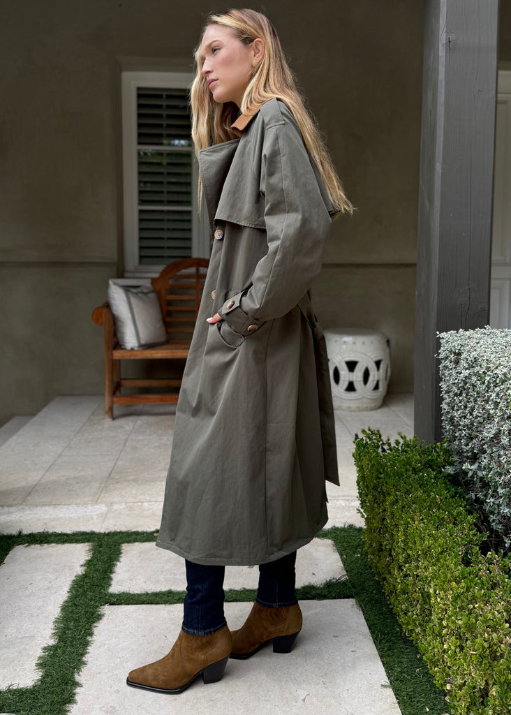 Woman in a long coat standing on a patio with a house in the background