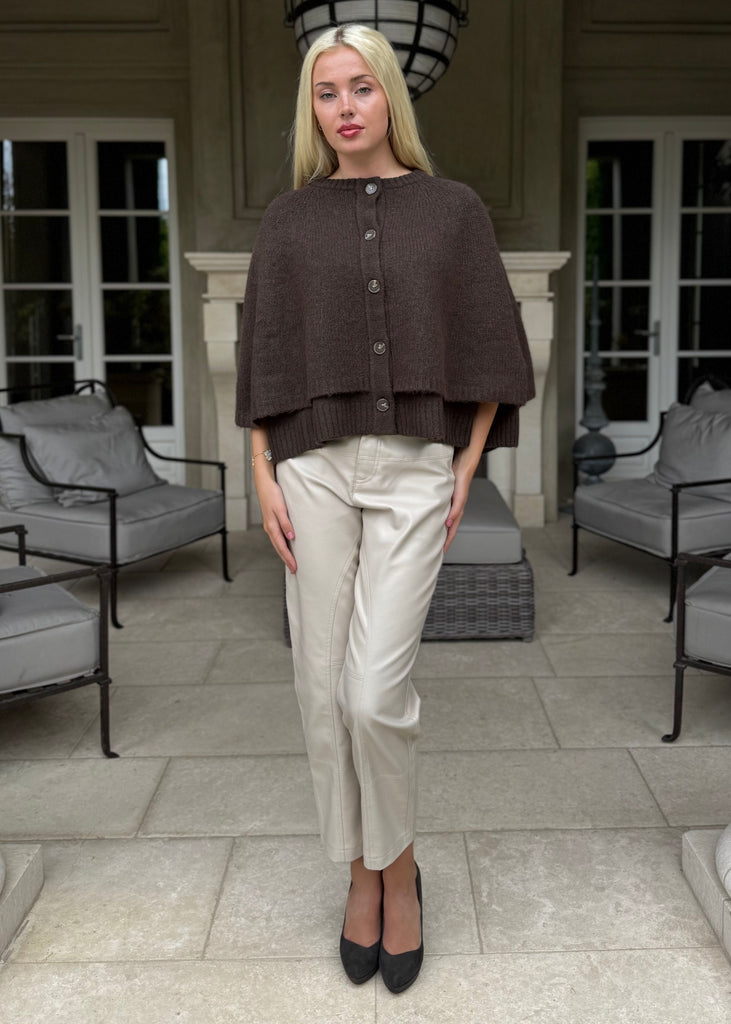 Woman standing in a stylish outdoor setting with columns and chairs.