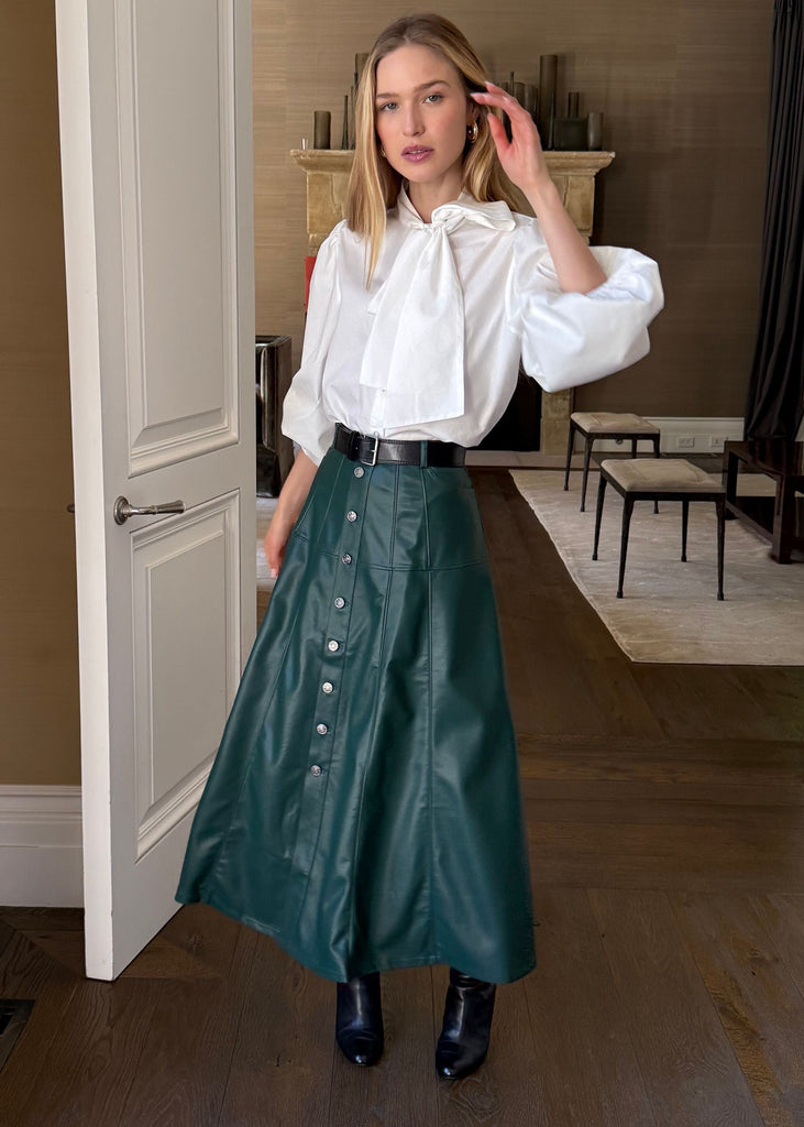 Woman in a white blouse and green skirt standing in a home interior.