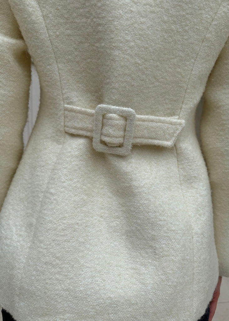 Close-up of a beige coat with a buckle detail on a plain background