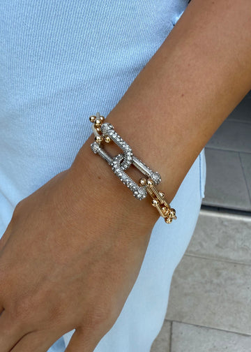Close-up of a wrist wearing a gold and silver bracelet against a light blue background.