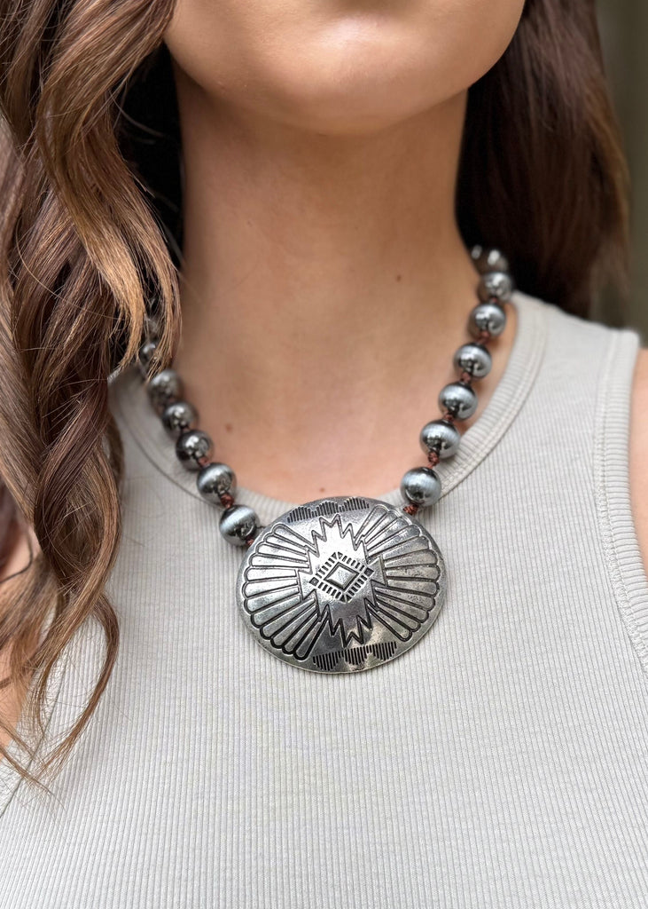 Woman wearing a silver necklace with a large pendant outdoors