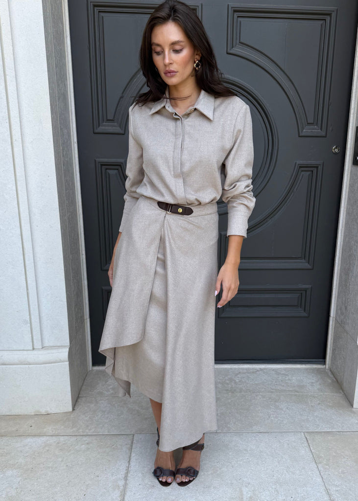 Woman in a beige shirt and skirt standing in front of a dark door.