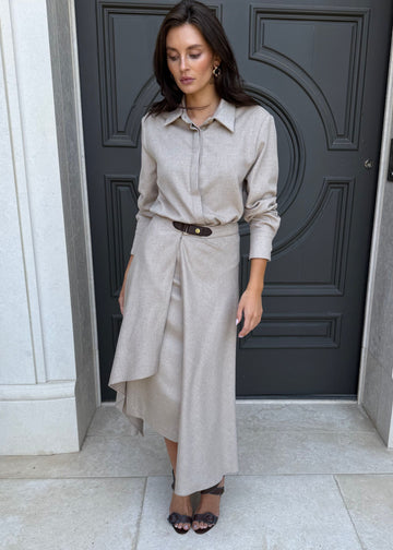 Woman in a beige shirt and skirt standing in front of a dark door.