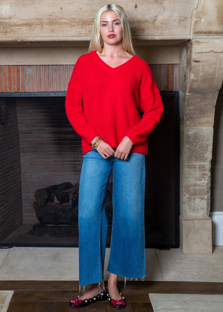Woman wearing a red sweater and blue jeans standing in front of a fireplace.