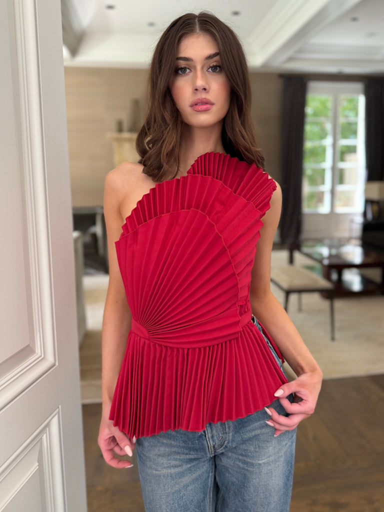 Woman wearing a red one-shoulder pleated top in a living room setting