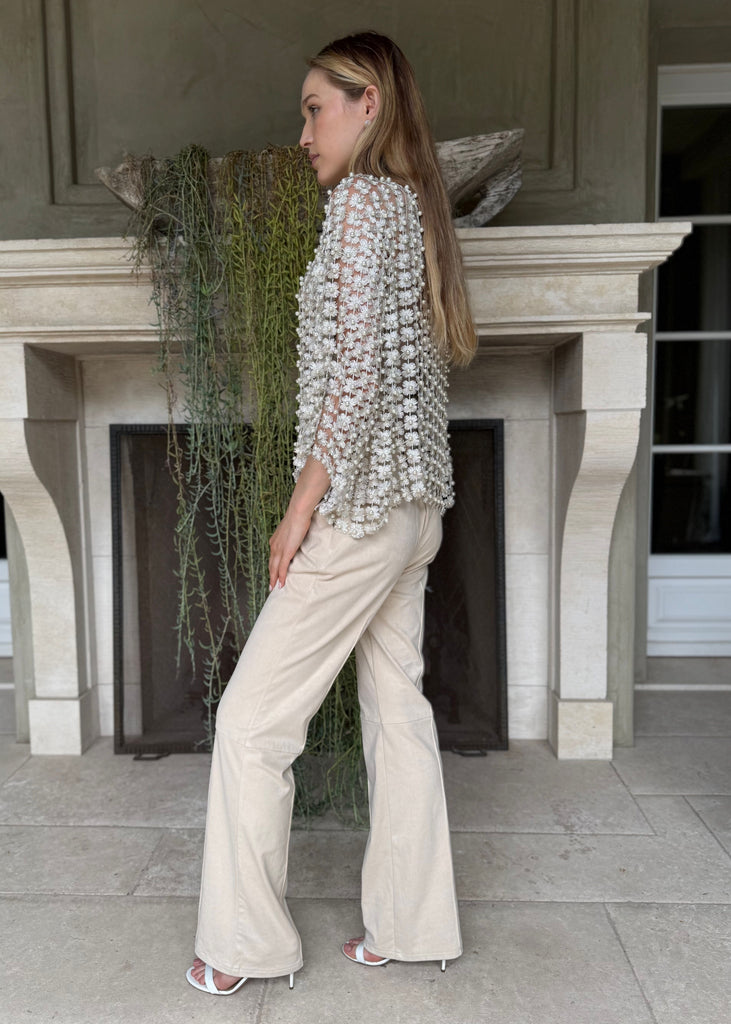Woman in a silver beaded top and beige pants standing in front of a fireplace.