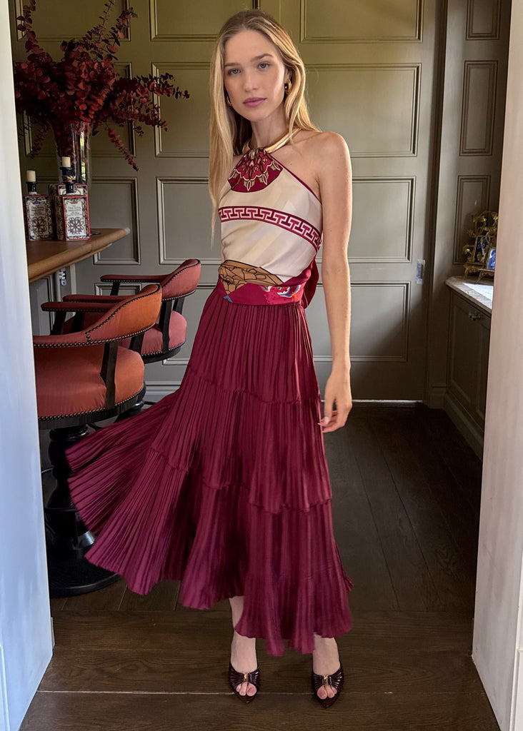 Woman in a red and white dress standing in a room with wooden flooring and a chandelier.