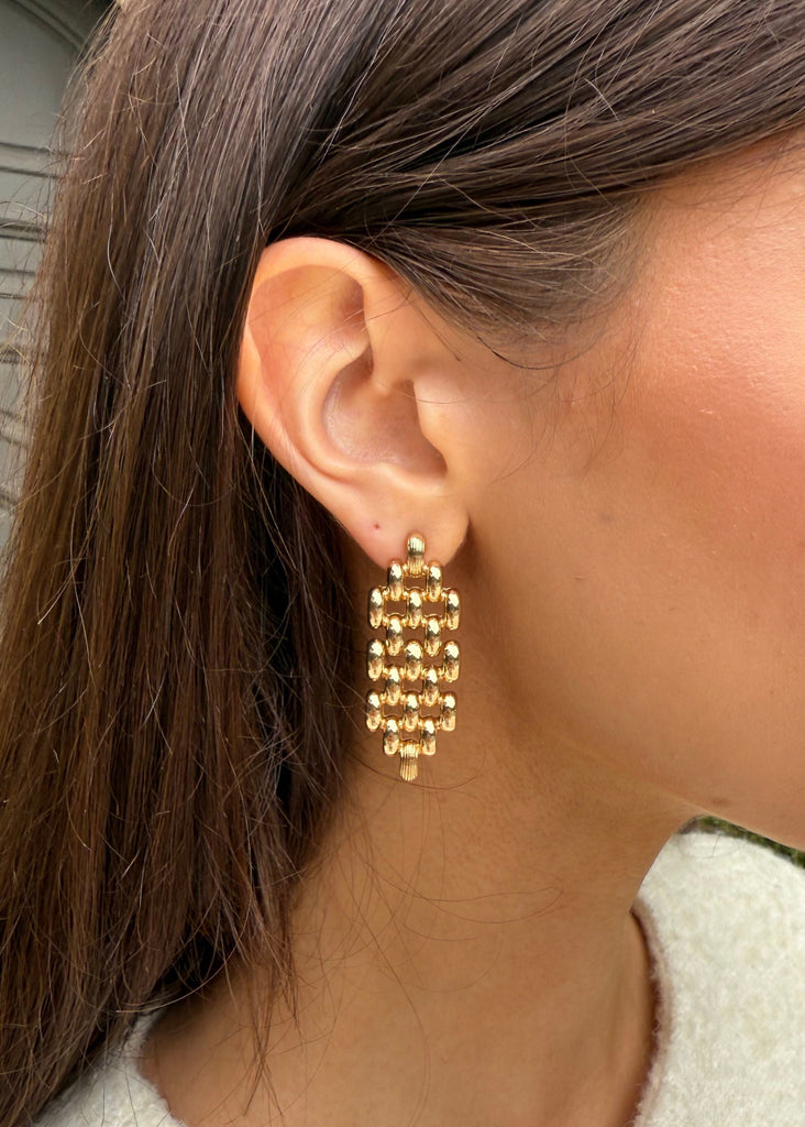 Close-up of a person wearing gold earrings with a neutral background